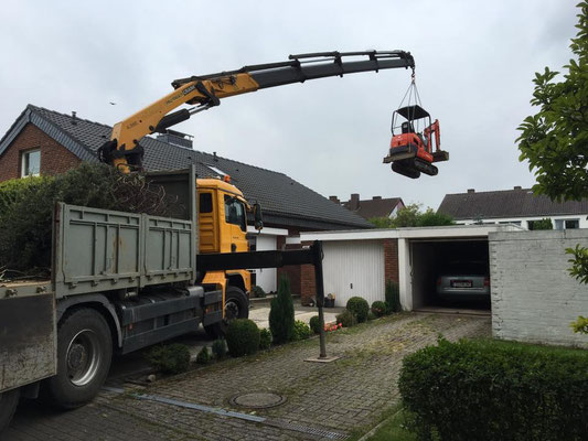 Minibagger wird mit LKW-Ladekran über ein Hindernis gehoben