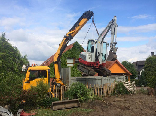 Minibagger wird mit dem LKW-Ladekran über eine Garage an die Einsatzstelle gehoben